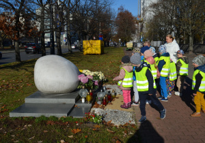 Dzieci z grupy Iv zapalają znicze przy kamieniu upamiętniającym Papieża Jana Pawła II, który znajduje się obok Pawiaka