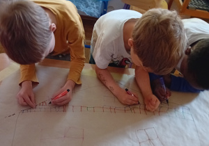 Dzieci z grupy III rysują na szarym papierze domek Pani Jesieni