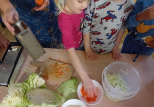 Dzieci z grupy III wsypują do pojemnika startą marchewkę